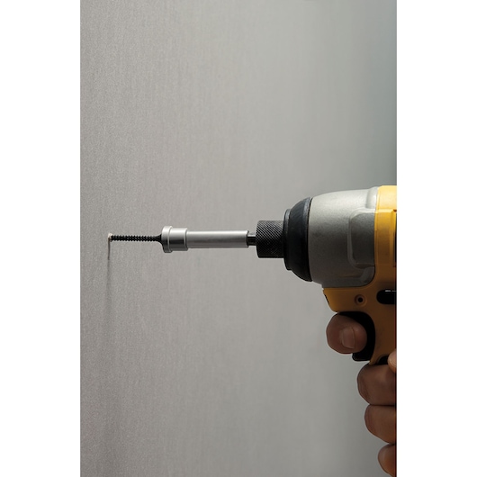 STANLEY STHT0-16137 screwdriver bit in drill driving screw into wall, side view.
