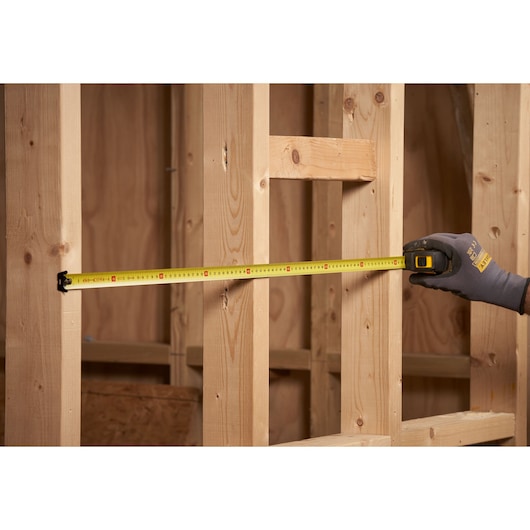 STANLEY STHT0-33559 tape measure measuring wooden framework in construction setting.