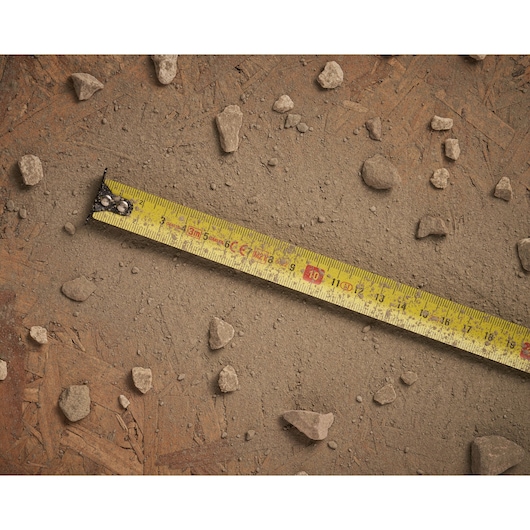 STANLEY STHT0-33559 yellow tape measure extended on dusty ground with scattered small rocks.