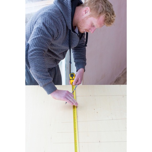 Photo of person using STANLEY STHT0-36118 tape measure to mark a line on a wooden board, top view.