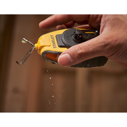 STANLEY STHT0-47147 chalk line reel in yellow and black held in a hand with chalk dust in midair.