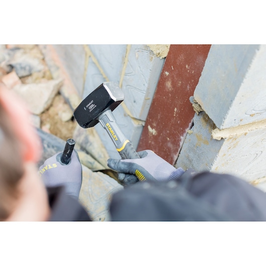 Stanley STHT0-54128 club hammer with grey rubber handle used by gloved worker on masonry wall.