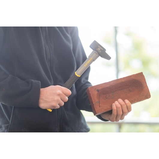 Photo of STANLEY STHT0-54131 club hammer with yellow handle held near a red brick.