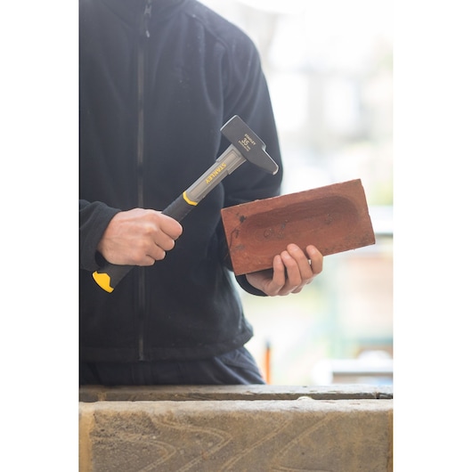 STANLEY STHT0-54154 hammer with black and yellow handle held by person in black jacket, used on red brick.