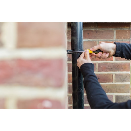 STANLEY STHT0-60308 screwdriver used to fix pipe bracket on brick wall outdoors.