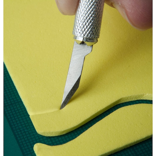 STANLEY STHT0-73872 precision craft knife cutting yellow foam on green surface, close-up angle.