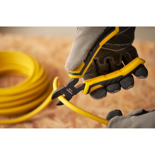 STANLEY STHT0-74362 pliers cutting yellow cable, close-up photography, person wearing gloves.