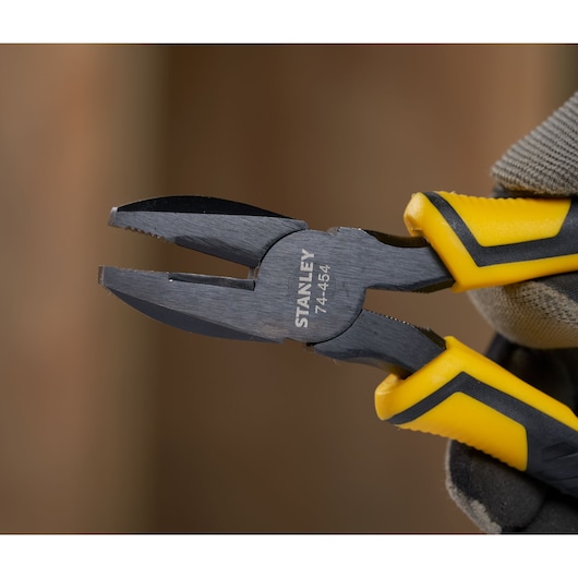 STANLEY STHT0-74367 combination pliers with black and yellow handles held in a gloved hand, close-up photo.