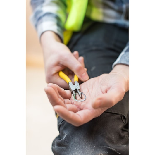 Photo of STANLEY STHT0-75413 pliers with yellow handles being used to hold a metal ring, close-up view.