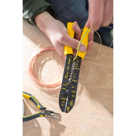 Photo of STANLEY STHT0-75414 wire stripper with yellow handles being used to strip wire, side view.