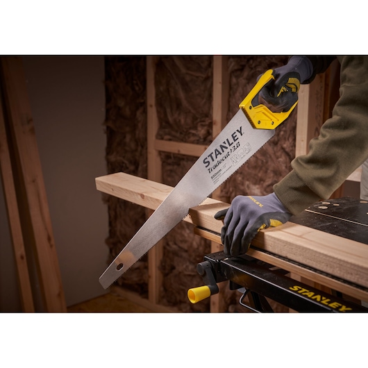 STANLEY STHT1-20352 hand saw with yellow handle cutting wooden beam in workshop setting.