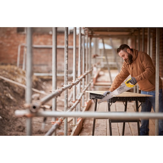 STANLEY STHT1-20352 hand saw in use on a construction site, cutting wood on a sawhorse table.