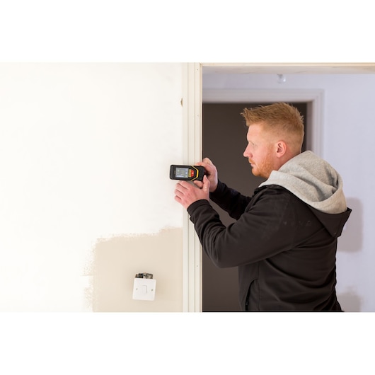Photo of STANLEY STHT1-77139 electronic detector used on a wall, person in black hoodie operating device.