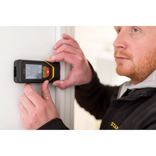 Photo of STANLEY STHT1-77139 laser distance measurer in use against a door frame, display shows measurement.