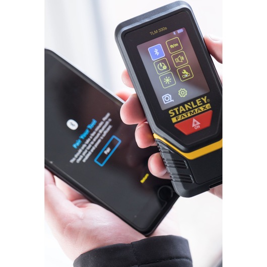 STANLEY STHT1-77140 laser distance measurer held near smartphone, close-up front view.