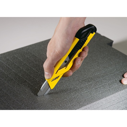 Photo of STANLEY STHT10265-0 utility knife cutting black foam sheet, close-up view of hand holding yellow knife.