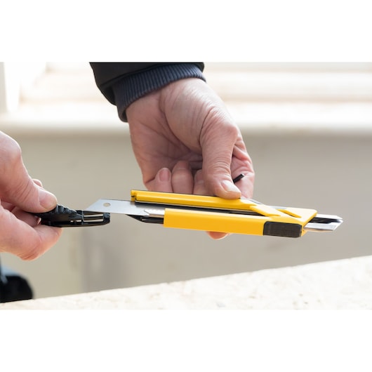 STANLEY STHT10266-0 utility knife with yellow handle being held in hand, indoor close-up photography.