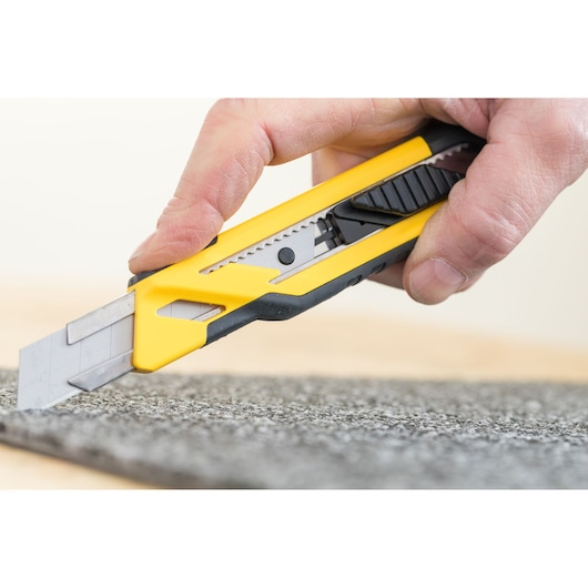 STANLEY STHT10266-1 utility knife with yellow and black body cutting carpet, close-up photography.