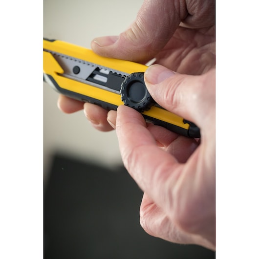 STANLEY STHT10268-1 utility knife with yellow and black body, close-up of adjustment wheel in hand