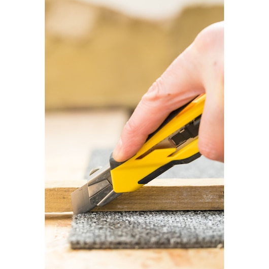 STANLEY STHT10270-0 utility knife cutting grey carpet, close-up photo of product in use.