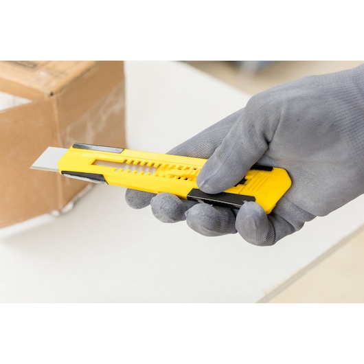 STANLEY STHT10345-0 utility knife with yellow handle held by gloved hand, box in background.