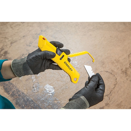 Photo of STANLEY STHT10364-0 utility knife with yellow handle, blade replacement, held by gloved hands.