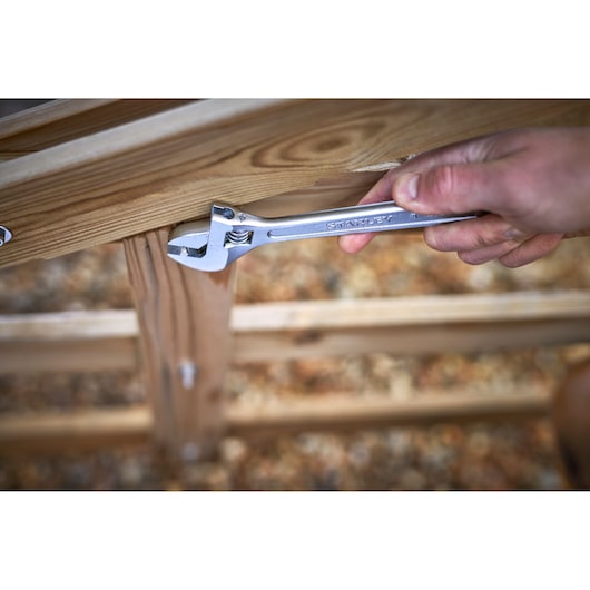 STANLEY STHT13123-0 adjustable wrench held by hand turning bolt on wooden structure outdoors.