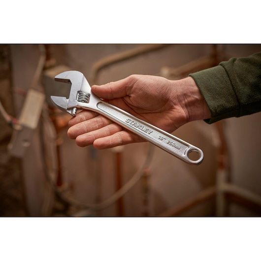 Photo of STANLEY STHT13123-0 adjustable wrench, 250mm size, held in hand against a background of pipes.