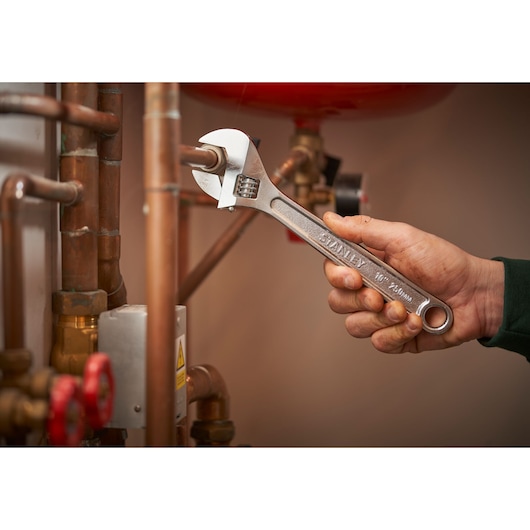 Stanley STHT13156-0 adjustable wrench used on copper pipes, close-up of tool in hand.