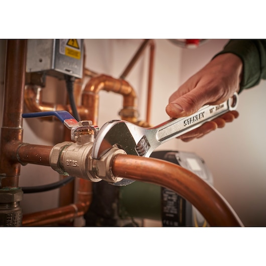 STANLEY STHT13156-0 adjustable wrench in use on copper plumbing pipes, close-up indoor photo.