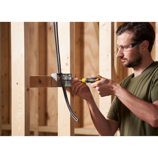 STANLEY STHT16155-0 screwdriver in use on electrical box, shown held by a person in woodworking construction.