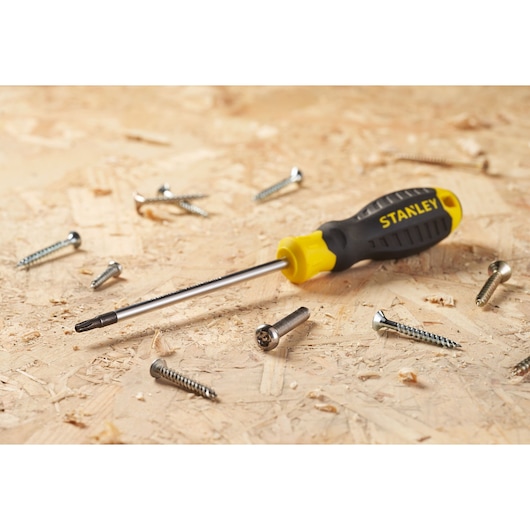 STANLEY STHT16179-0 screwdriver with black and yellow handle on wood surface, surrounded by metal screws, side angle.