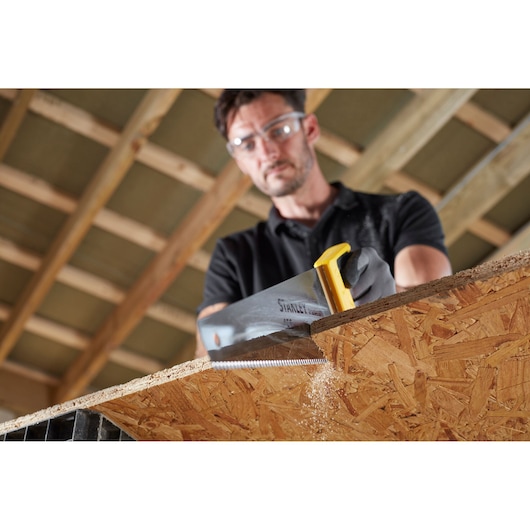 STANLEY STHT20354-1 hand saw with yellow handle, cutting wooden panel in carpentry setting.