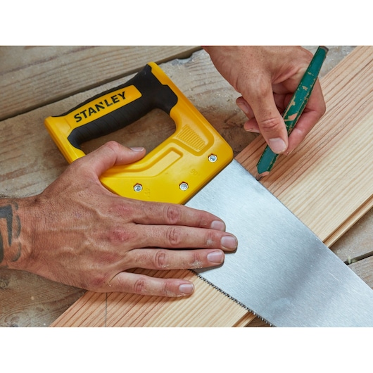 STANLEY STHT20371-1 hand saw with yellow and black handle held on wood, person marking cut line.
