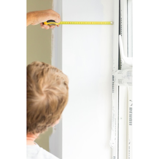 STANLEY STHT36802-0 tape measure in use measuring a white wall near a window, close-up angle.