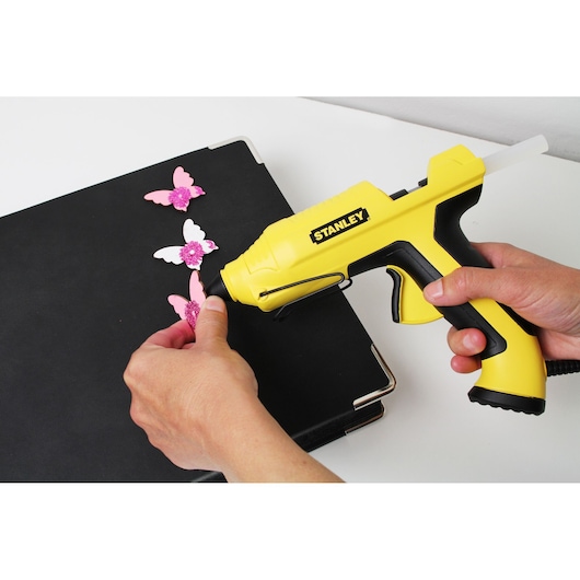 STANLEY STHT6-70417 yellow glue gun used for crafting pink butterfly decorations on a black folder.