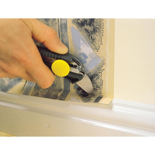 STANLEY STHT7-10220 wallpaper cutter with yellow dial, shown cutting wallpaper near trim.