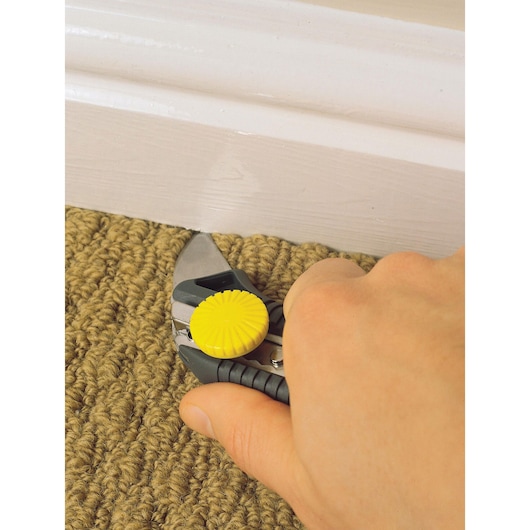 Photo of STANLEY STHT7-10220 utility knife cutting carpet near baseboard.