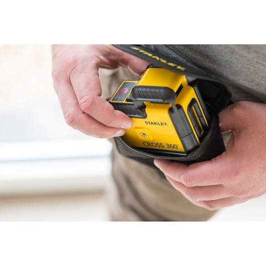 STANLEY STHT77504-1 yellow CROSS 360° laser level being placed into a black carrying pouch by hand.