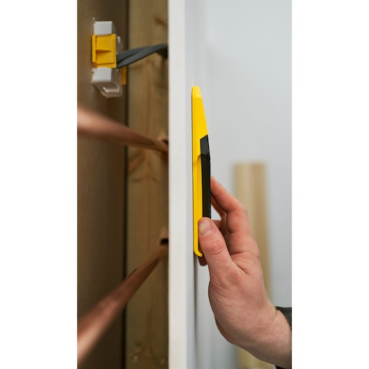STANLEY STHT77588-0 yellow stud finder held against wall, close-up side angle, electrical wires in background