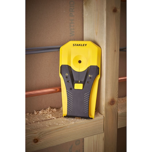 Stanley STHT77588-0 stud finder, yellow and black, angled vertically on wooden stud, photography.