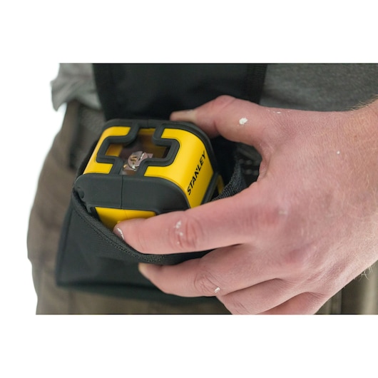 STANLEY STHT77649-1 yellow laser level held in hand, being placed into a black pouch, close-up view.