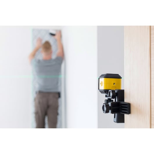 STANLEY STHT77649-1 laser level tool mounted on door frame, person working in background.