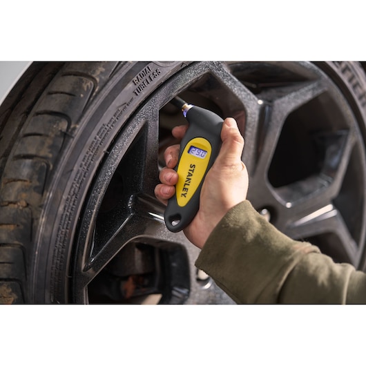 STANLEY STHT80874-0 digital tire pressure gauge in hand measuring car tire pressure.