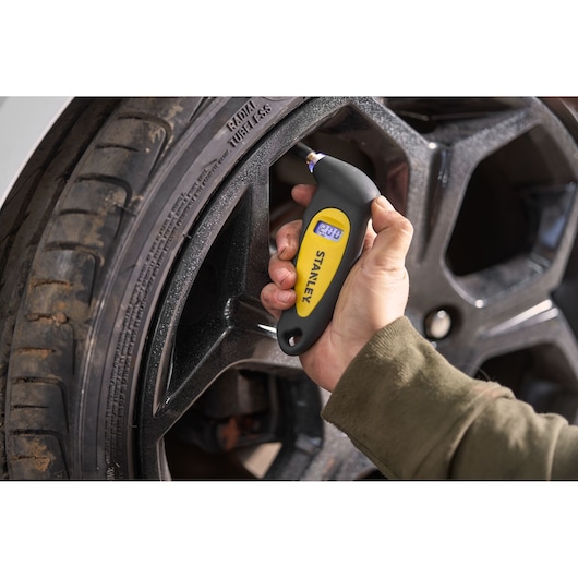 STANLEY STHT80874-0 digital tire pressure gauge checking car tire, close-up photography.