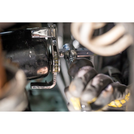 Photo of STANLEY STHT80880-0 ratchet wrench tightening bolt in automotive engine, gloved hand visible.