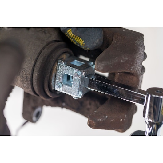 STANLEY STHT80883-0 brake caliper tool in use on rusty car brake assembly, close-up view.