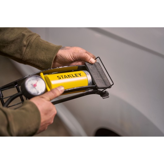 STANLEY STHT80894-1 yellow foot pump with pressure gauge held in hand near vehicle.