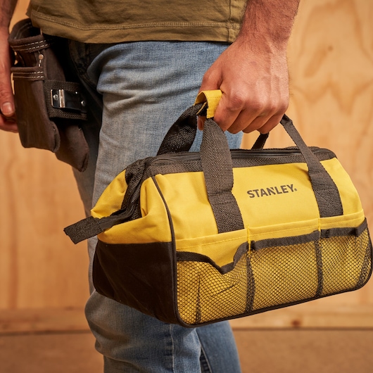 STANLEY STMT0-74101 yellow and black tool bag with mesh pockets, shown being carried by hand.