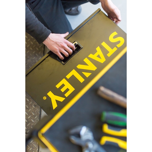 Photography of STANLEY STMT1-74305 toolbox with yellow logo, person holding handle, tools in foreground.